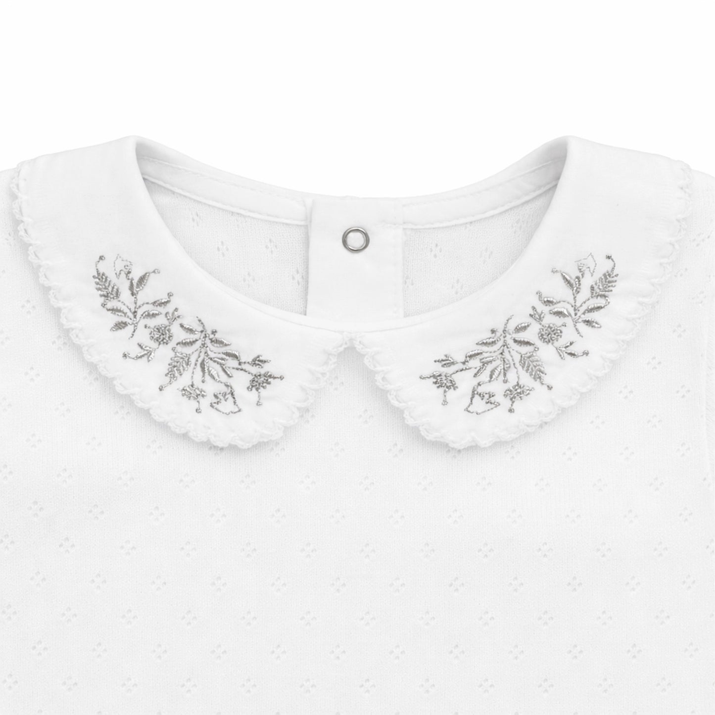 Close-up of Maison Leopolda Noe baby body showing silver leaf-and-bird embroidery on white cotton pointelle