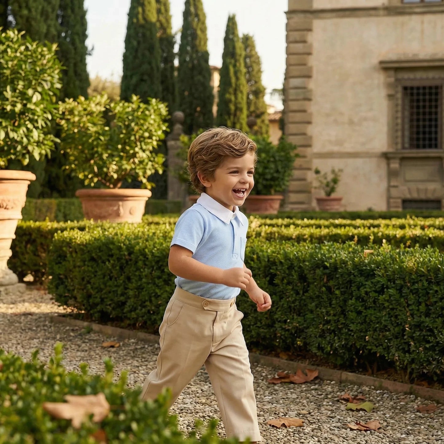Boy wearing Maison Leopolda Oscar Polo Shirt in light blue and Henry Trousers in beige running through an Italian villa garden with manicured hedges and terracotta planters