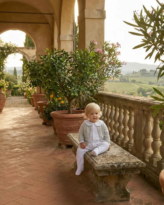 Child sitting on a stone bench in an outdoor setting with potted plants and a scenic background.